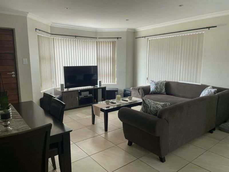 Spacious open-plan living and dining area featuring neutral tiled flooring, recessed lighting, and a large bay window with vertical blinds.
