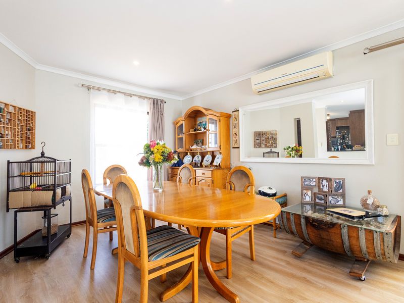 A well-lit dining room featuring laminate flooring, coving, and a wall-mounted split-system air conditioner.