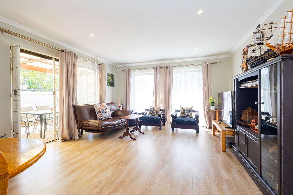 Bright and spacious living room featuring light-toned laminate flooring, recessed downlighting, and large sliding glass doors providing direct access to the outdoor patio area.