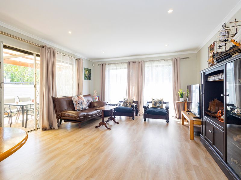 Bright and spacious living room featuring light-toned laminate flooring, recessed downlighting, and large sliding glass doors providing direct access to the outdoor patio area.