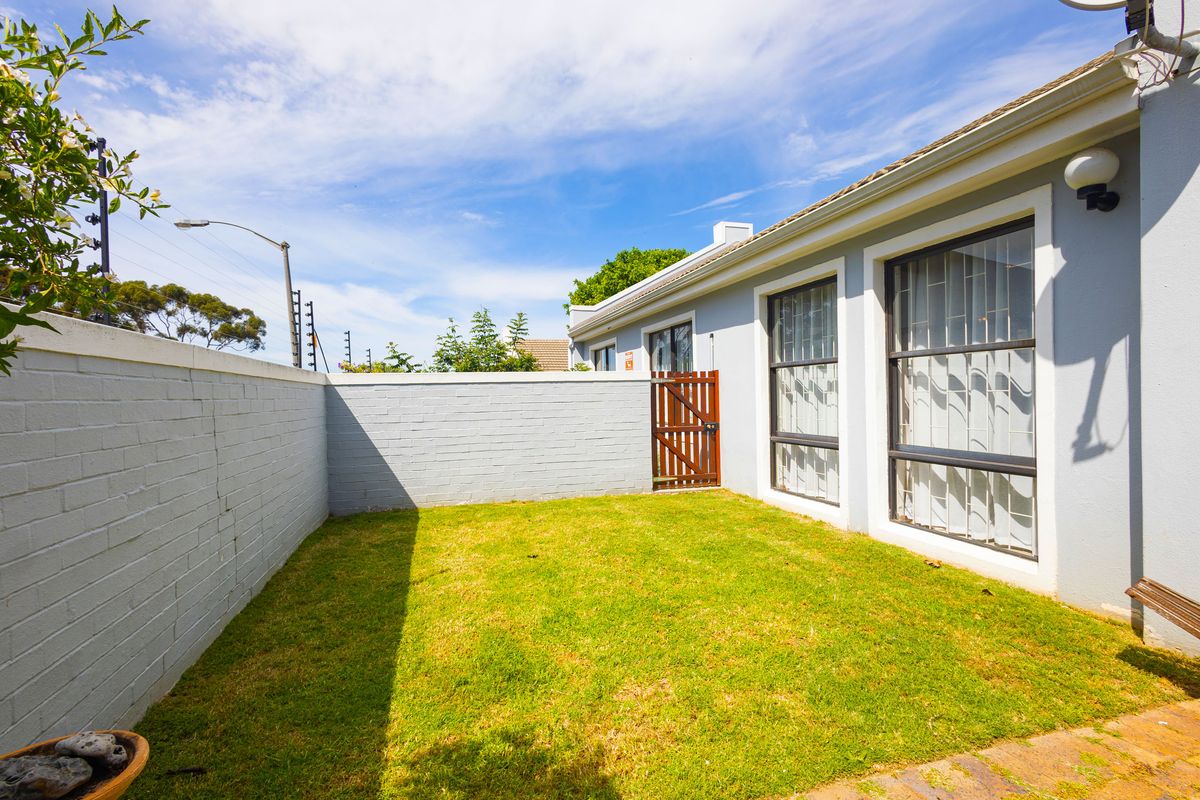 A private rear garden area featuring a lawn, brick boundary wall with security fencing, and a wooden pedestrian gate.