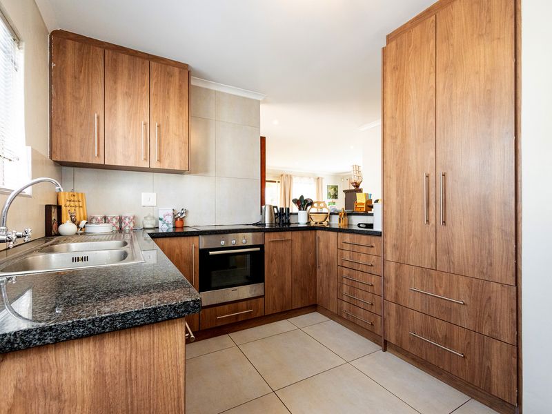 A well-maintained kitchen featuring wood-finish cabinetry, granite countertops, a built-in oven, and neutral tiled flooring, offering a functional and clean workspace.
