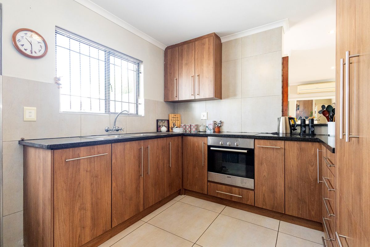 A functional kitchen featuring wood-finish cabinetry, granite countertops, a built-in oven, and tiled flooring with a window providing natural light.