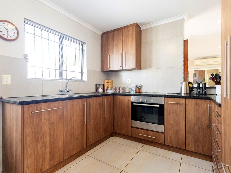 A functional kitchen featuring wood-finish cabinetry, granite countertops, a built-in oven, and tiled flooring with a window providing natural light.