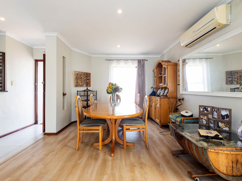 A well-maintained dining room featuring light-toned laminate flooring, recessed downlighting, and a wall-mounted split-system air conditioning unit.
