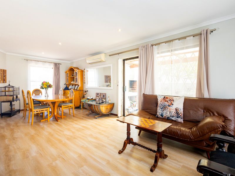 Spacious open-plan living and dining area featuring light laminate flooring, recessed lighting, and a split-system air conditioner with direct access to the patio.