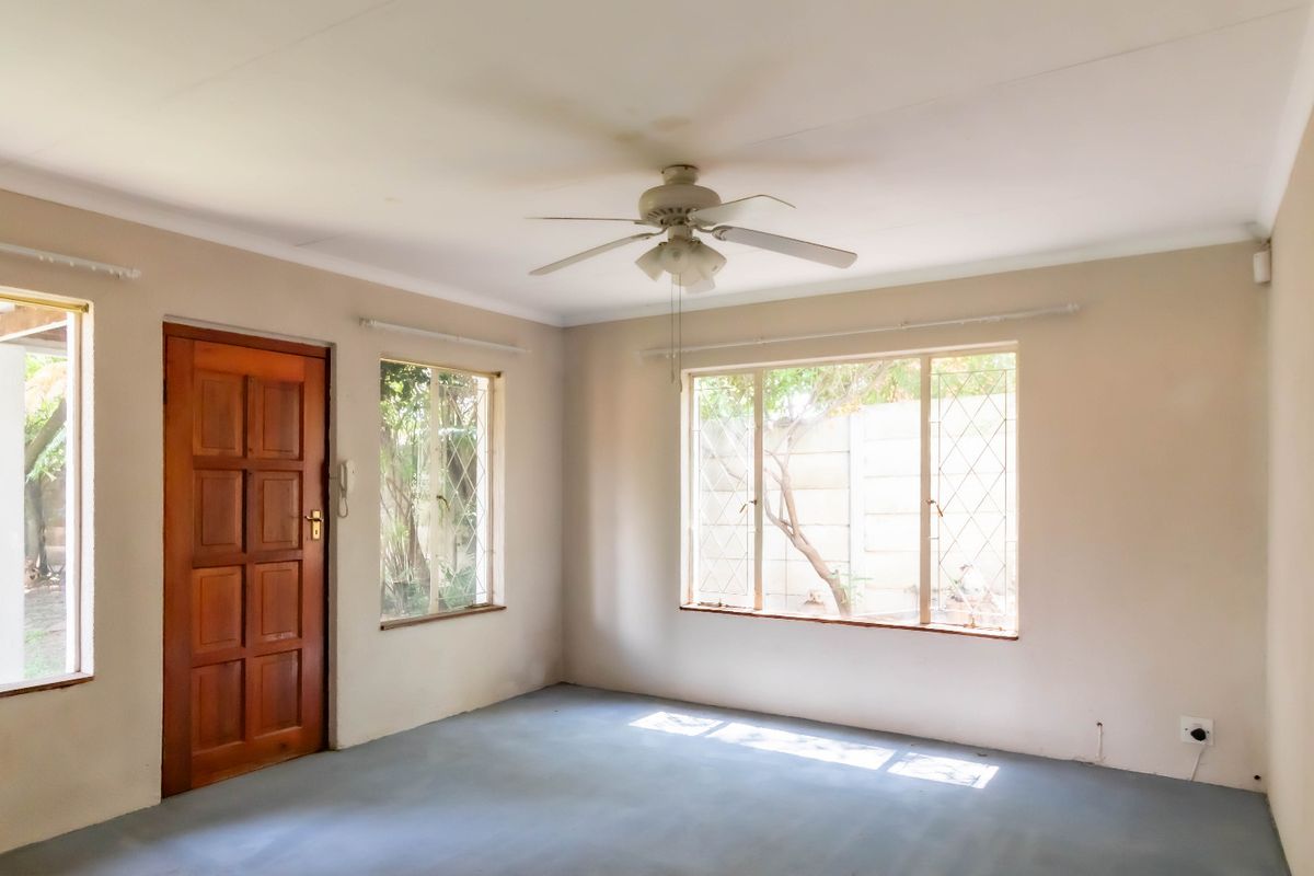 An empty living room featuring a ceiling fan, security bars on the windows, and a solid wood door leading to the exterior.