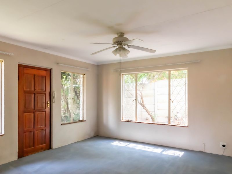 An empty living room featuring a ceiling fan, security bars on the windows, and a solid wood door leading to the exterior.