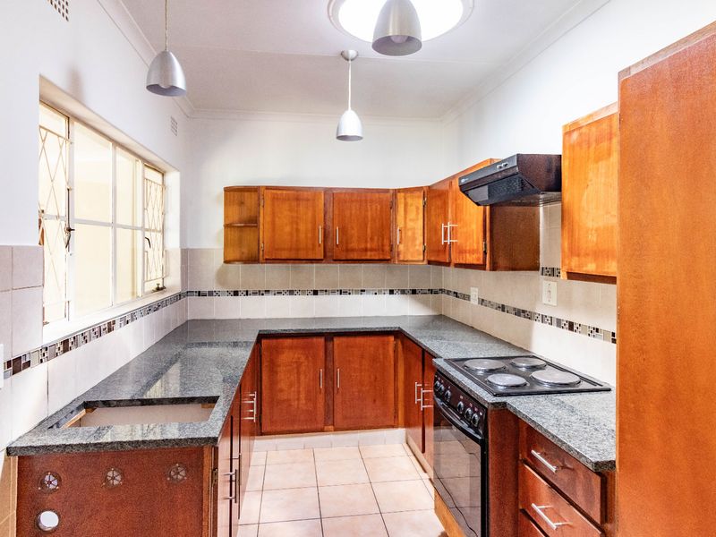 A functional kitchen featuring wooden cabinetry, granite countertops, a built-in oven with hob, and a tiled backsplash. The space is currently vacant.