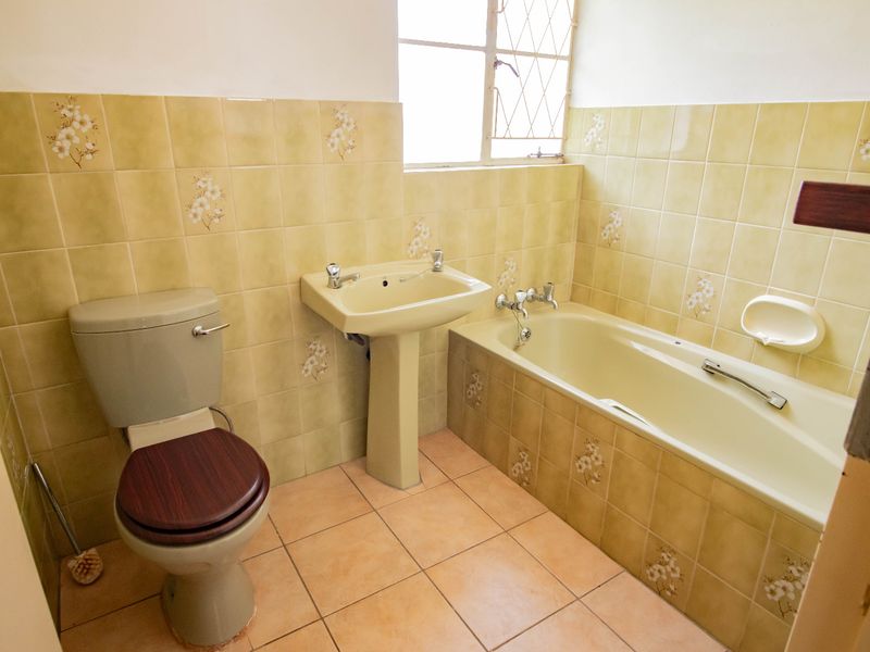A dated bathroom featuring a pedestal basin, bathtub, and toilet with original floral-patterned wall tiles and ceramic flooring.