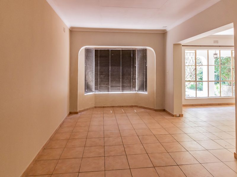 An empty, open-plan living area featuring neutral tiled flooring, a distinctive bay window with blinds, and an arched transition to an adjacent space.