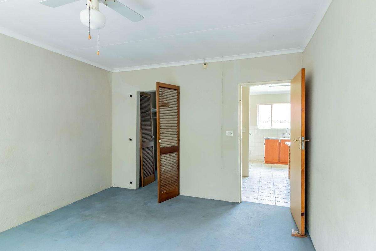 An empty bedroom featuring a ceiling fan, louvered closet doors, and direct access to an adjacent kitchen area.