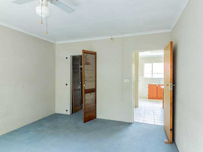 An empty bedroom featuring a ceiling fan, louvered closet doors, and direct access to an adjacent kitchen area.
