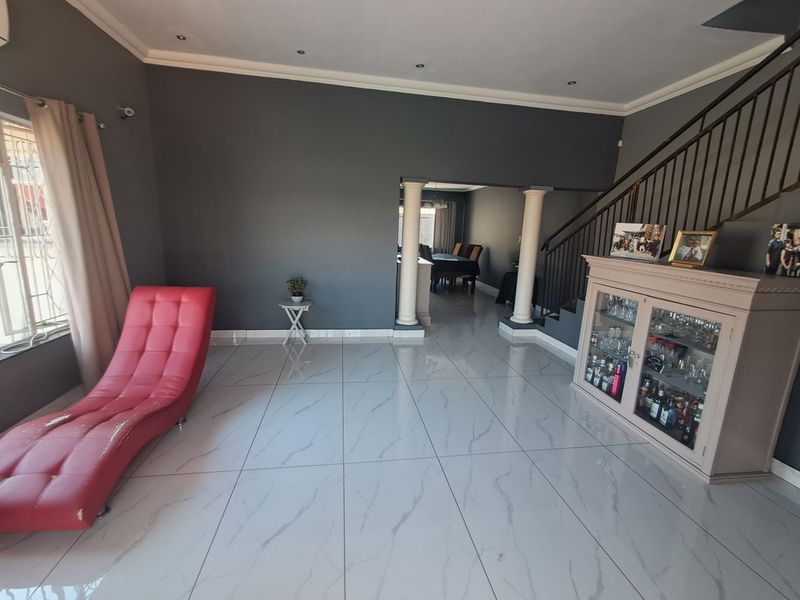 Spacious living area featuring polished marble-look floor tiles, decorative columns, and an open-plan transition to the dining room with a staircase.