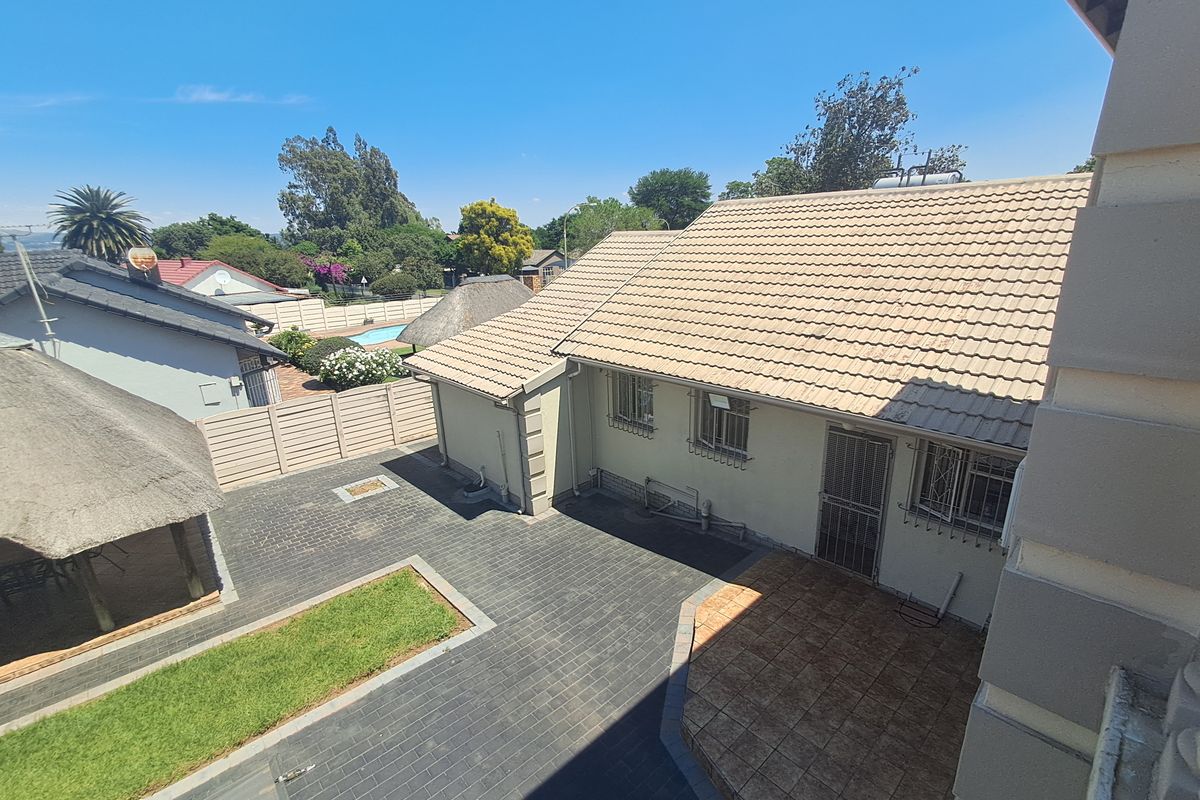 Elevated view of the rear exterior featuring a paved courtyard, tiled roof, and a detached thatched lapa area within a secure boundary.