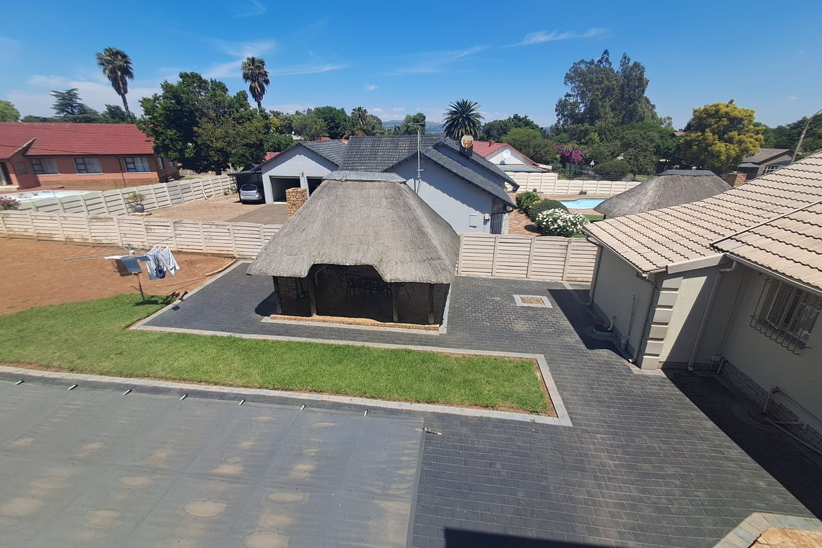 Aerial view of the property backyard featuring a paved patio area, a thatched lapa, a swimming pool with cover, and surrounding boundary walls.