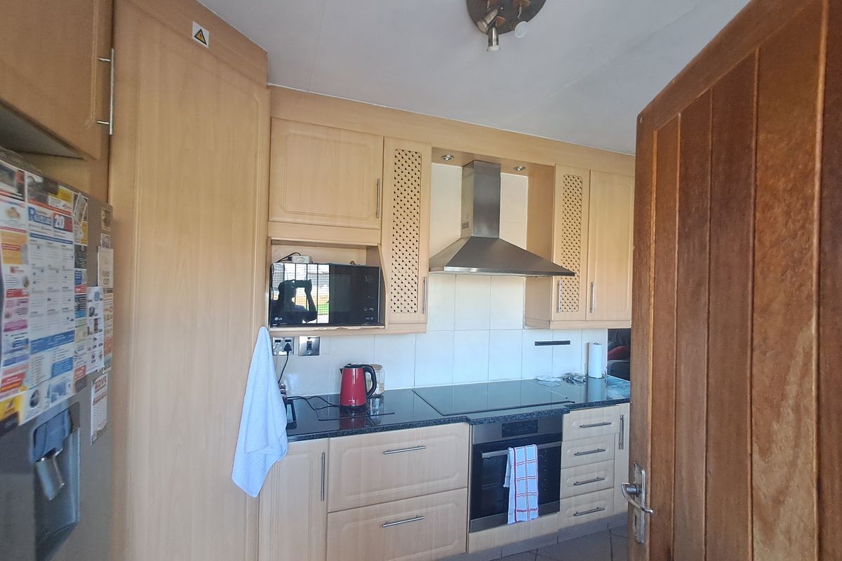 A functional kitchen featuring light-wood cabinetry, granite countertops, a built-in oven with a ceramic hob, and a stainless steel extractor fan.