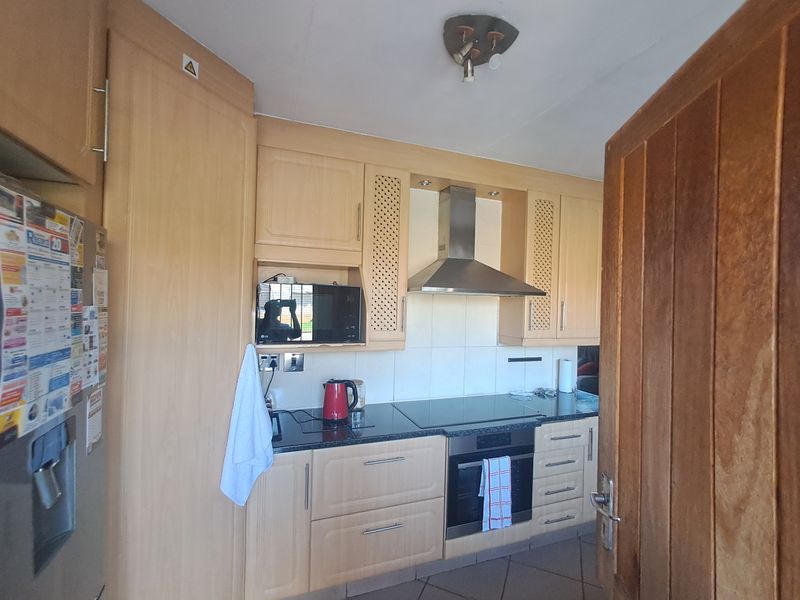 A functional kitchen featuring light-wood cabinetry, granite countertops, a built-in oven with a ceramic hob, and a stainless steel extractor fan.