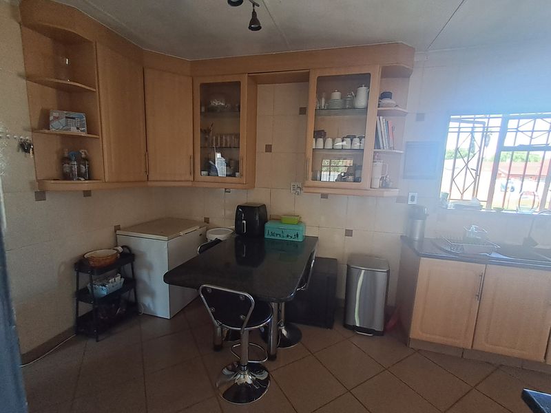 A dated kitchen featuring wooden cabinetry, tiled backsplash, and tiled flooring, offering a functional layout with potential for modern renovation.