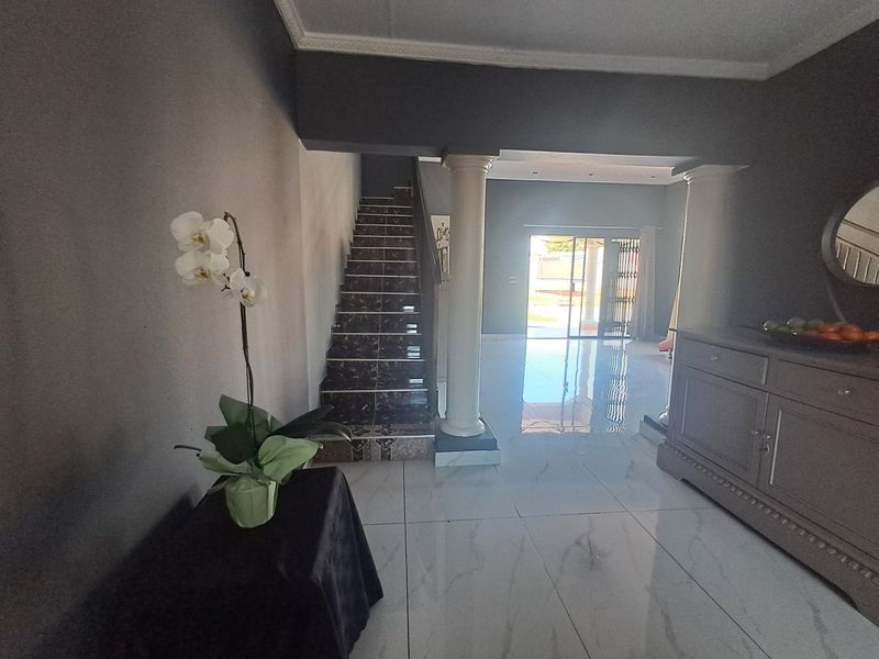 Spacious living area featuring polished tiled flooring, decorative columns, and a staircase leading to the upper level, with access to the outdoor area.