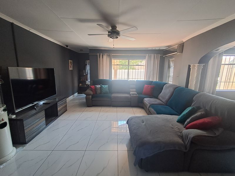 Spacious living room featuring large format floor tiles, a ceiling fan, and an integrated air conditioning unit with neutral wall finishes.