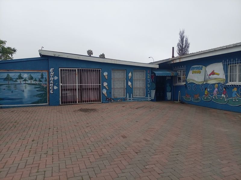 Front exterior view of a commercial or educational property featuring a paved driveway, security bars on windows, and painted mural facade.
