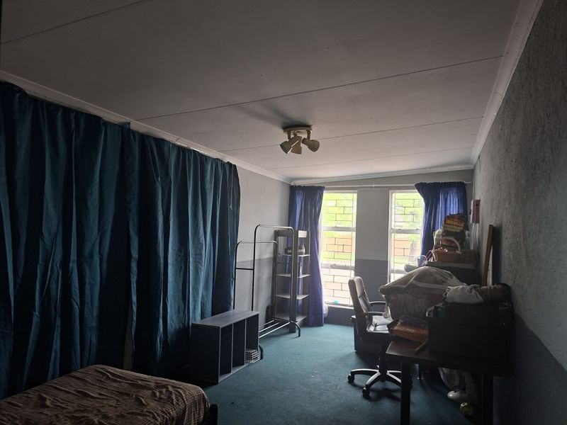 A bedroom featuring carpeted flooring, steel frame windows, and a central ceiling light fixture, requiring cosmetic updates to improve the overall aesthetic.