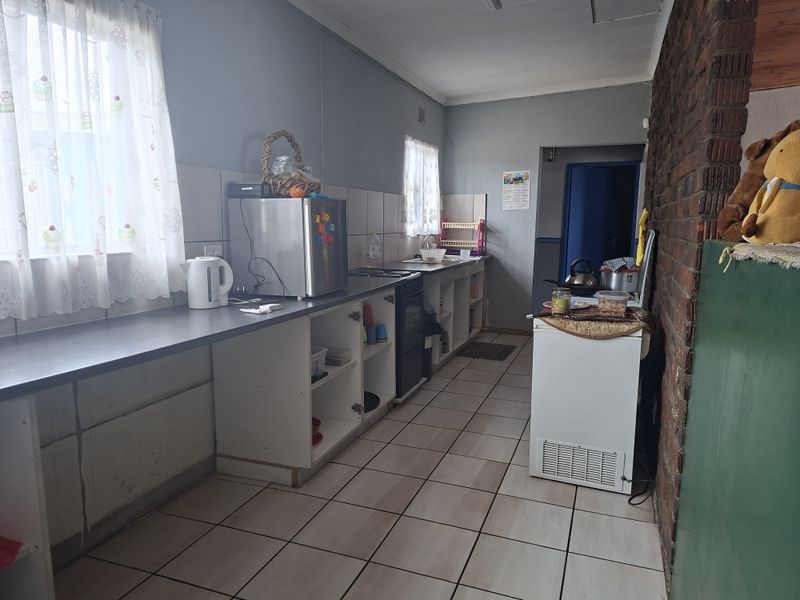 A functional kitchen featuring tiled flooring, an exposed brick feature wall, and open-shelf cabinetry with a built-in stove and sink area.