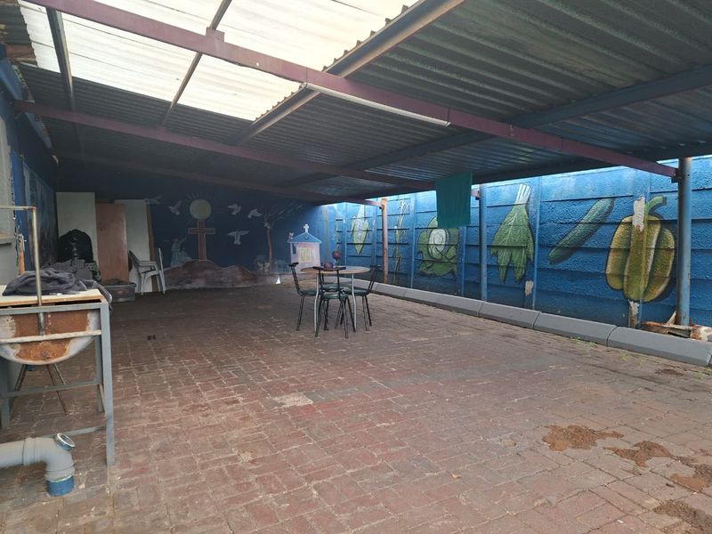 A covered outdoor patio area featuring brick paving, a corrugated metal roof, and precast concrete walls with decorative murals.
