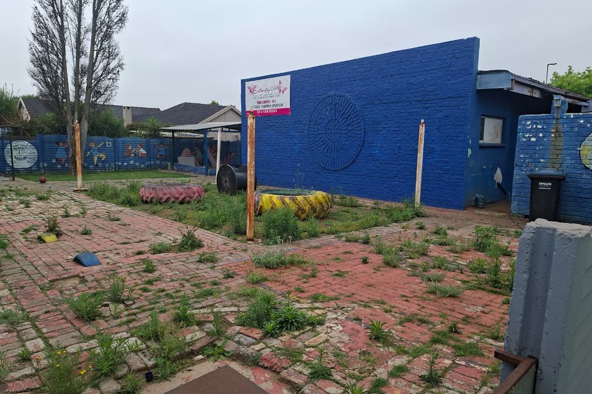 Rear exterior area featuring brick paving and a painted brick wall, currently showing signs of neglect and significant weed growth.