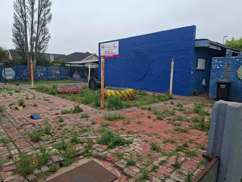 Rear exterior area featuring brick paving and a painted brick wall, currently showing signs of neglect and significant weed growth.