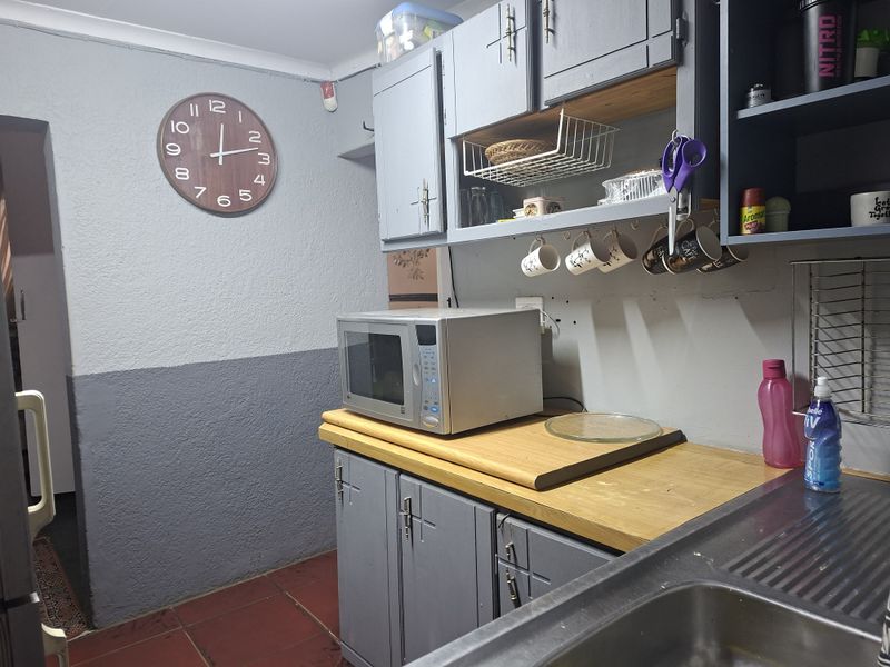 A functional kitchen area featuring built-in grey cabinetry, a wooden countertop, and a stainless steel sink, requiring cosmetic updates to improve its aesthetic appeal.