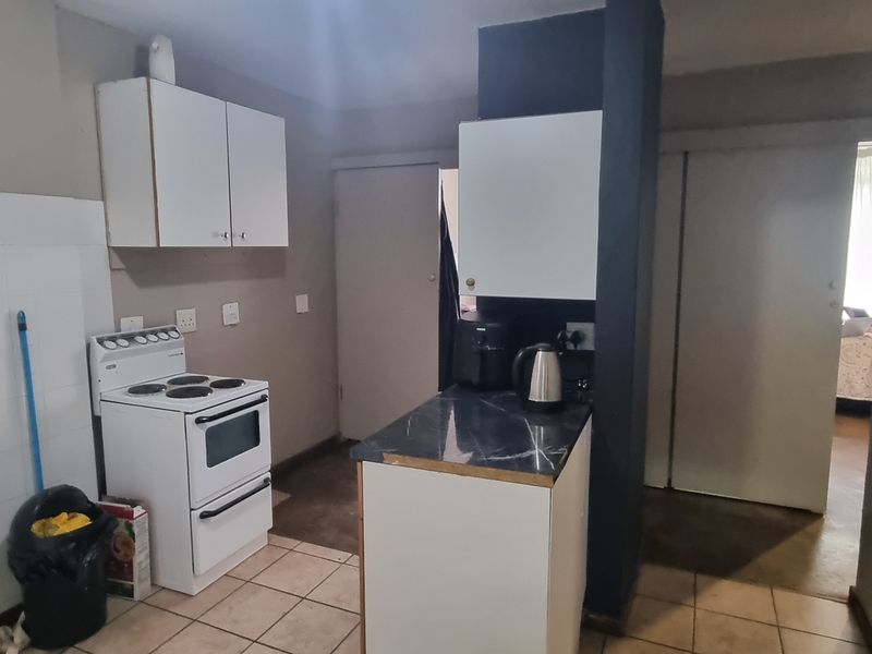 A compact kitchen featuring tiled flooring, white cabinetry, and a tiled splashback, offering a functional layout with potential for modern updates.