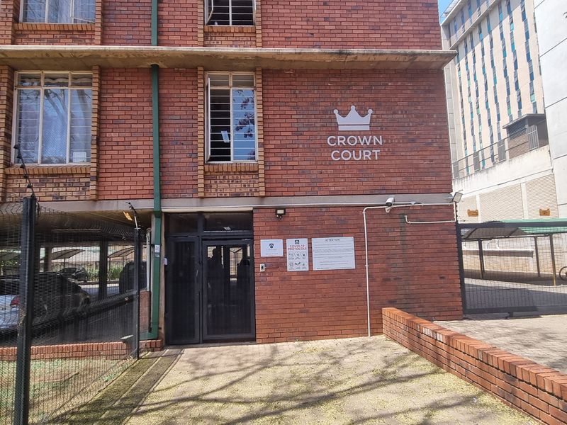 Front exterior view of Crown Court apartment building featuring face brick facade, secure entrance, and covered parking facilities.