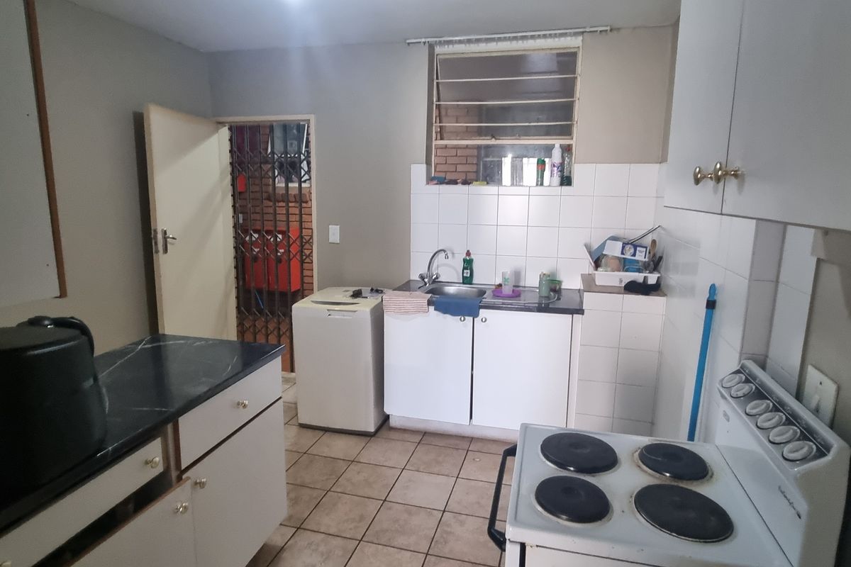 A functional kitchen featuring built-in cabinetry, a stainless steel sink, tiled splashbacks, and an electric stove, with direct access to a secure rear entrance.