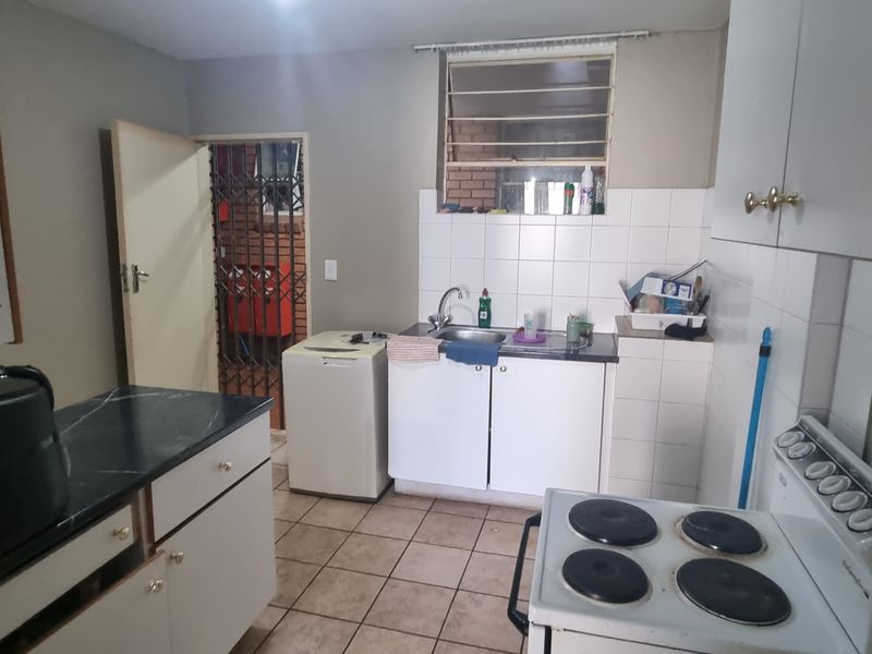 A functional kitchen featuring built-in cabinetry, a stainless steel sink, tiled splashbacks, and an electric stove, with direct access to a secure rear entrance.