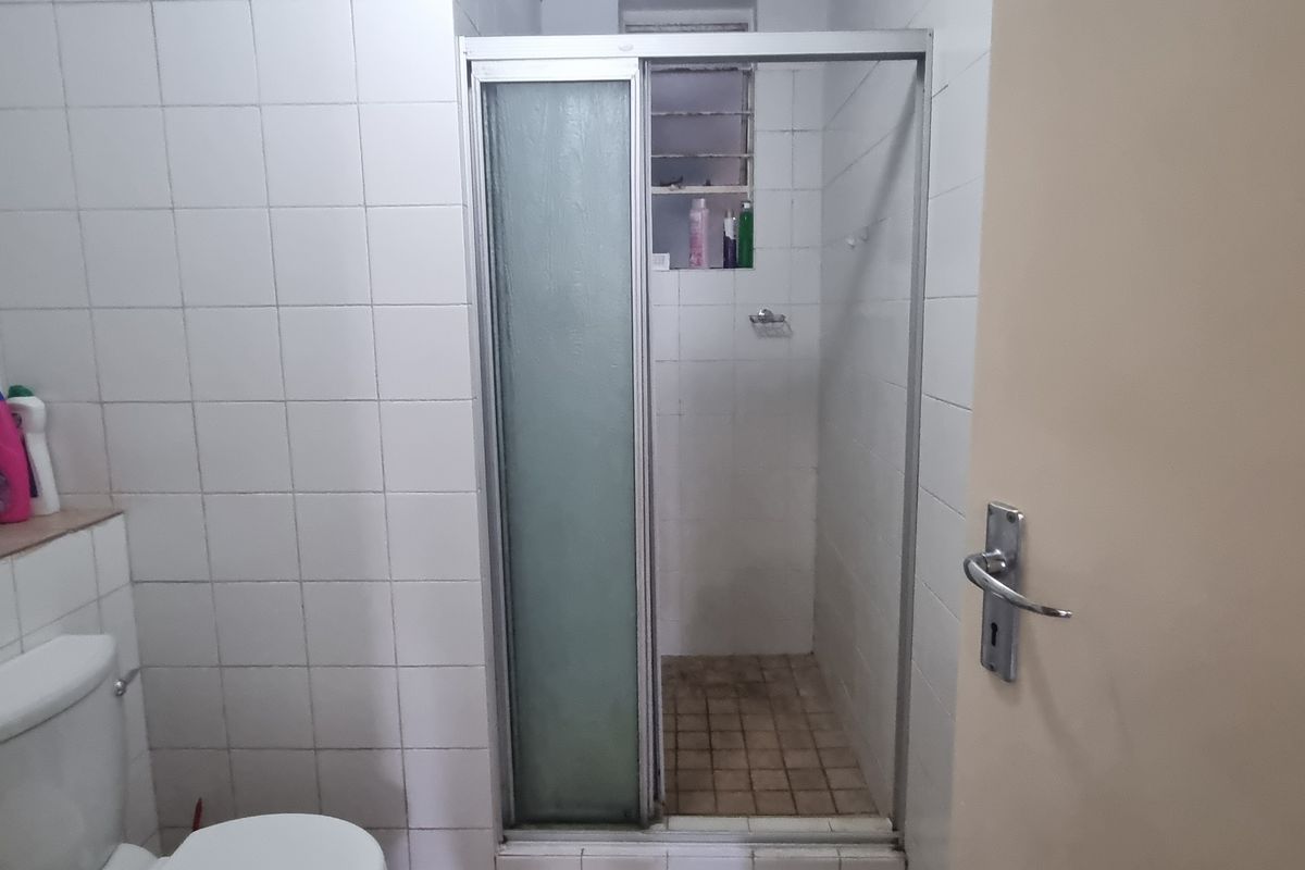 A functional bathroom featuring a shower enclosure with a glass door, a standard toilet, and white wall tiling throughout.