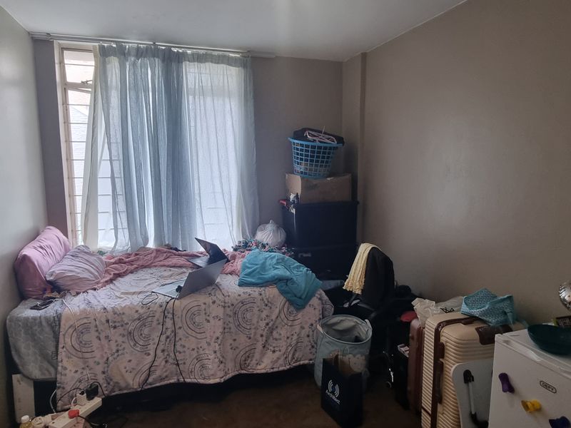 A compact bedroom featuring a window with curtain rails, requiring cosmetic updates to the walls and flooring to improve its overall appeal.