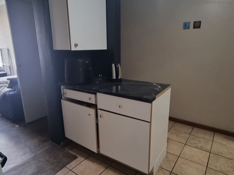 A compact kitchen area featuring basic cabinetry, a laminate countertop, and tiled flooring, adjacent to a bedroom space.