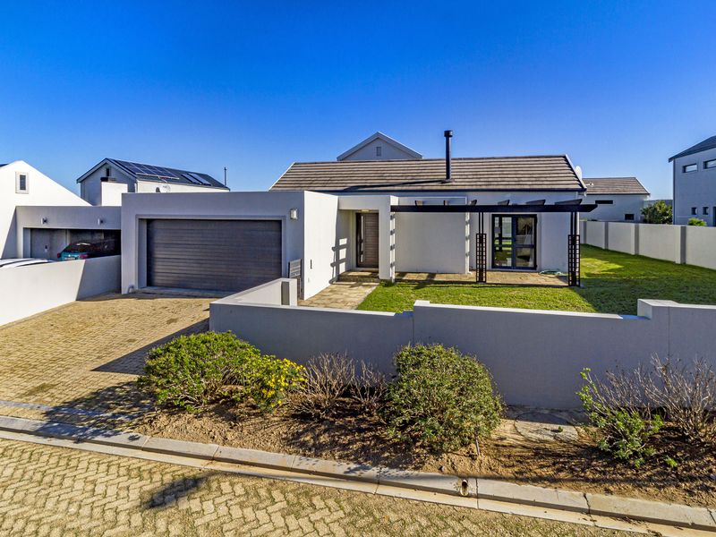 A modern single-story residential property featuring a paved driveway, integrated garage, and a front garden with a pergola-covered entrance area.