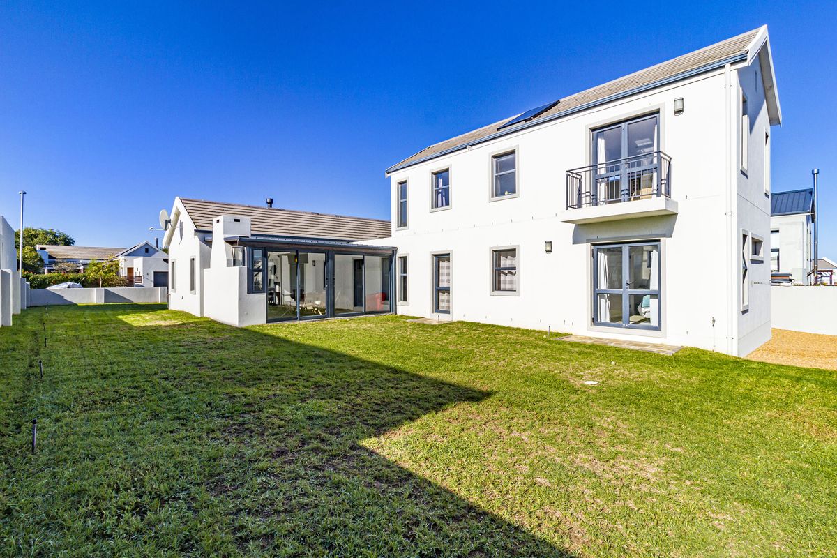Rear view of a two-story residential house featuring a private garden, balcony, and modern sliding glass doors.