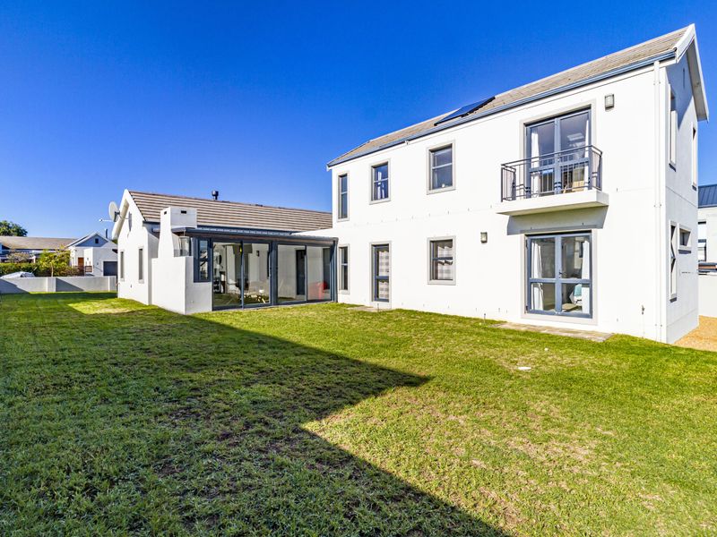 Rear view of a two-story residential house featuring a private garden, balcony, and modern sliding glass doors.
