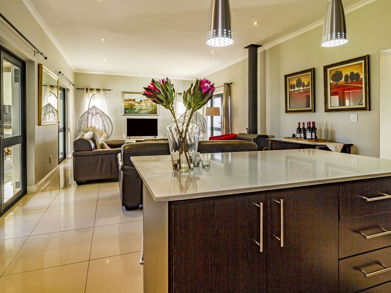 Spacious open-plan living area featuring a modern kitchen island with stone countertops, tiled flooring, a cozy fireplace, and seamless access to the outdoor patio.
