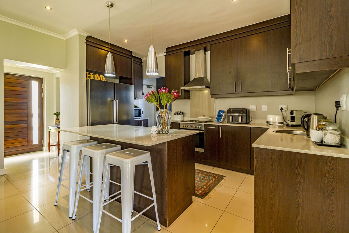 Modern kitchen featuring dark wood cabinetry, stone countertops, a central island, and integrated stainless steel appliances, complemented by recessed and pendant lighting.