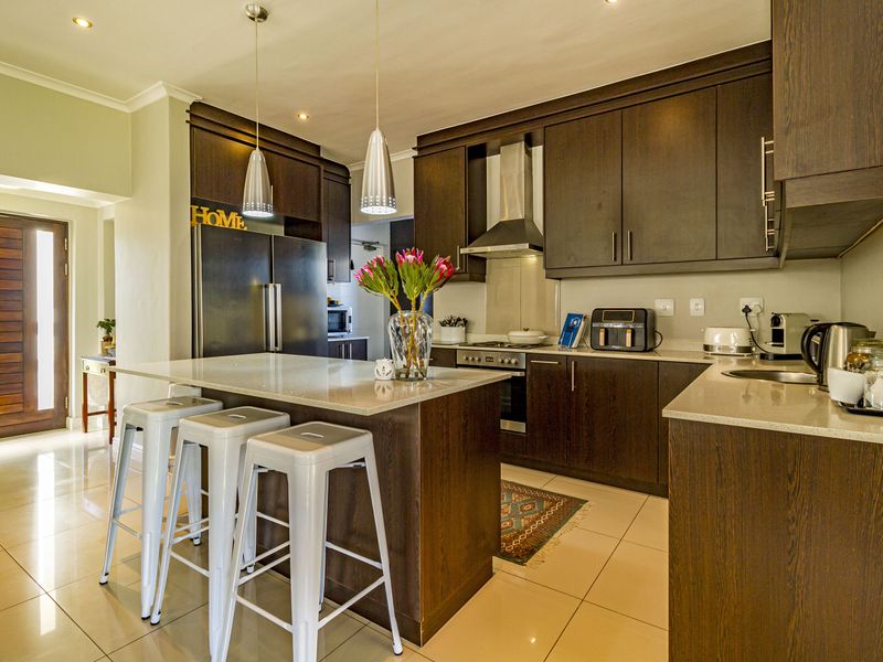 Modern kitchen featuring dark wood cabinetry, stone countertops, a central island, and integrated stainless steel appliances, complemented by recessed and pendant lighting.