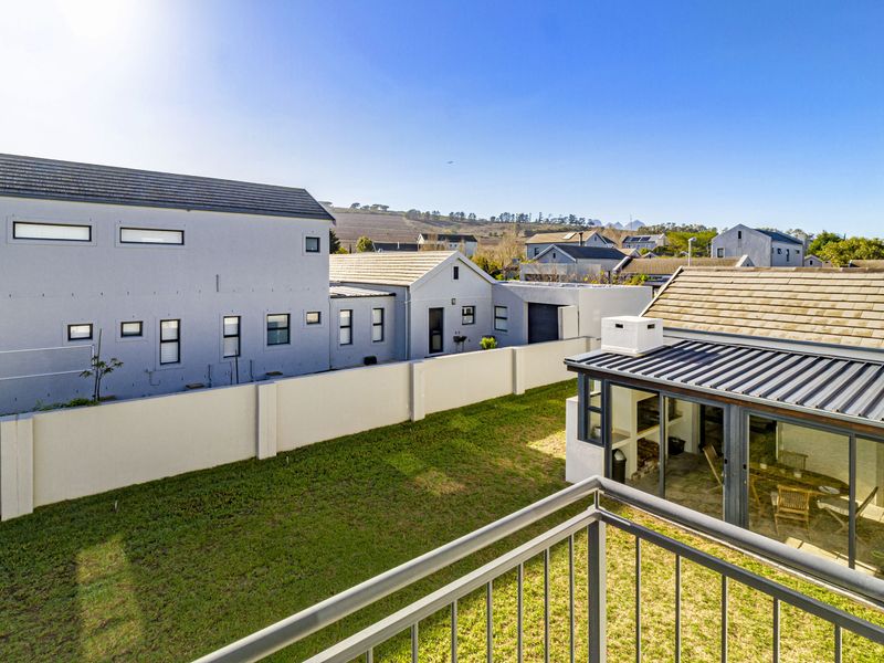 Elevated view of a rear garden featuring a lawn, boundary wall, and a covered patio area with a built-in braai.