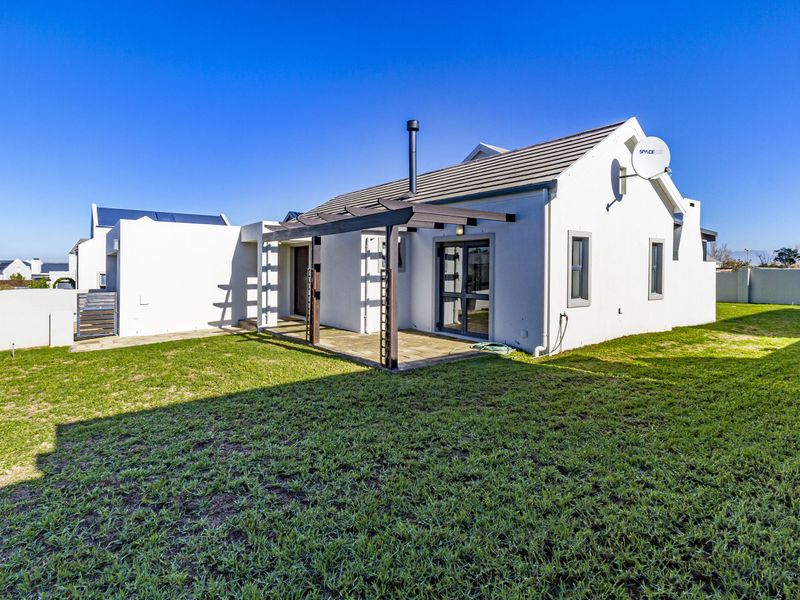 Rear view of the house featuring a paved patio area with a wooden pergola, a well-maintained lawn, and a tiled roof structure.