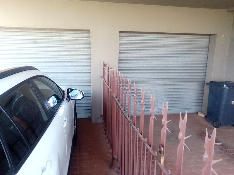 A double garage featuring roller doors and a paved driveway area secured by a metal fence.