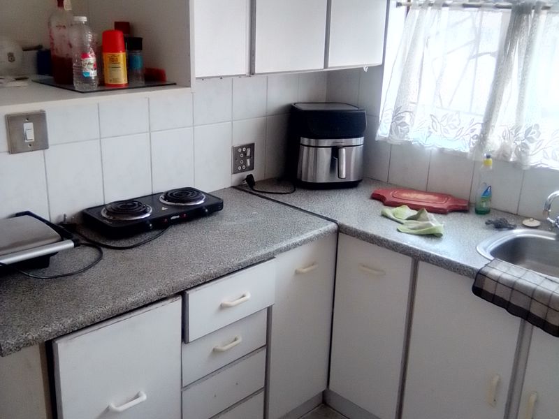 A compact kitchen featuring white cabinetry, laminate countertops, tiled backsplash, and ceramic flooring, offering a functional layout with potential for modern updates.