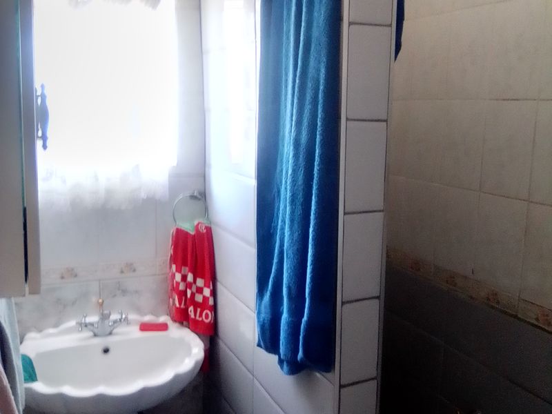 A compact bathroom featuring a pedestal basin and a tiled shower partition, requiring cosmetic updates to the wall finishes and grout.